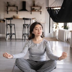 A woman meditates peacefully on a yoga mat indoors, promoting mindfulness and relaxation.