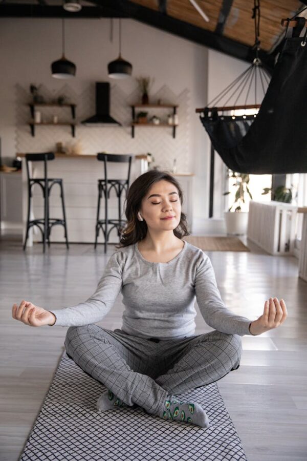 A woman meditates peacefully on a yoga mat indoors, promoting mindfulness and relaxation.